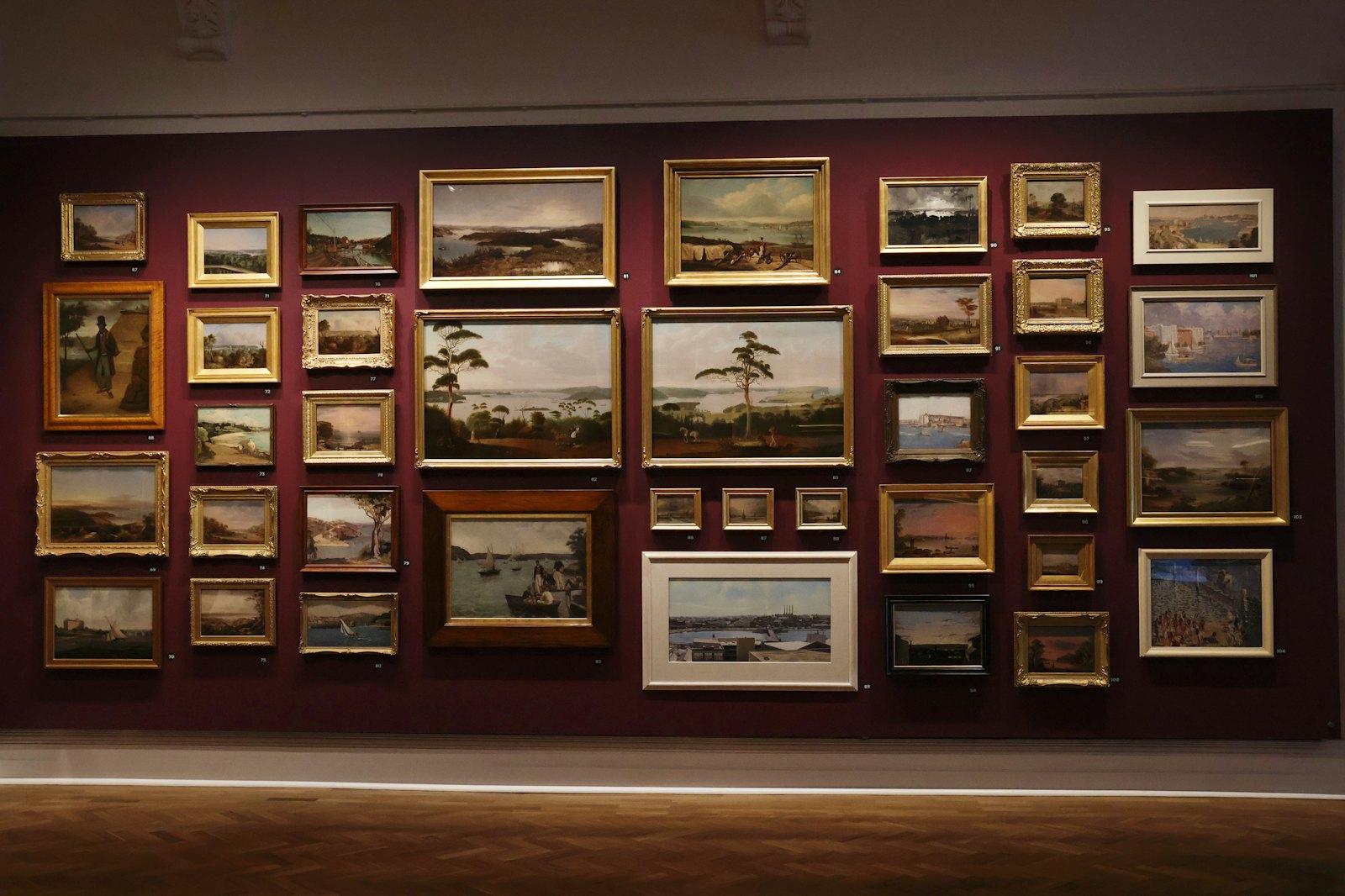 Landscape paintings hung salon-style across a deep red gallery wall.