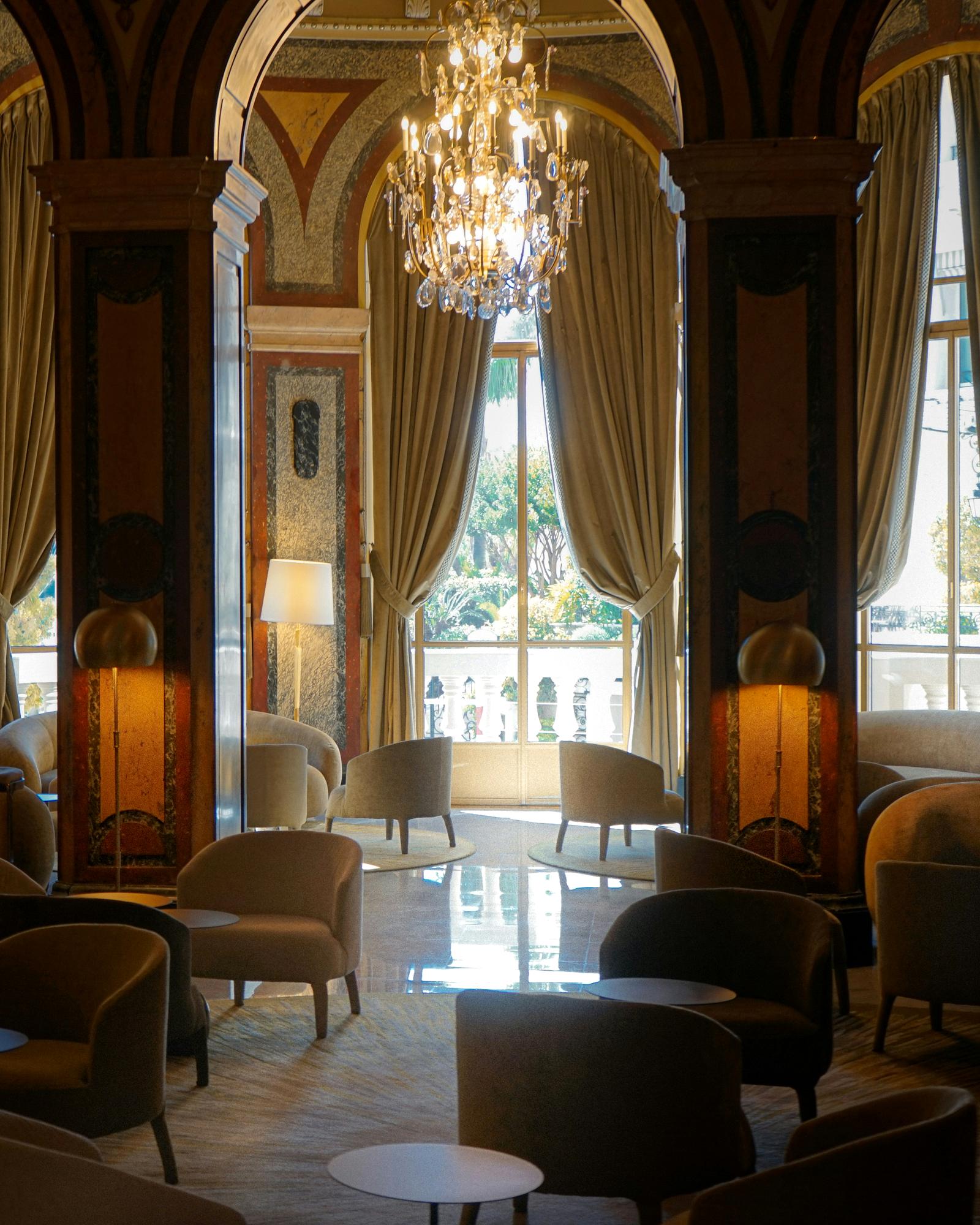 Intimate lounge inside a distinctive boutique hotel, with a crystal chandelier and armchairs arranged beneath an arched, painted ceiling.